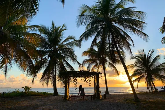 Mulher sentada apreciando o pôr do sol na praia de Maceió